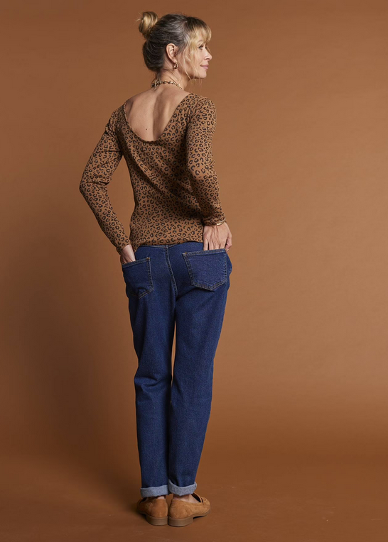 Woman wearing a leopard print top and blue jeans against a brown background