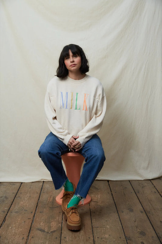 Person wearing a sweater with colorful text sitting on a stool against a plain background